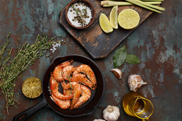 Grilled shrimps in cast iron pan with lime, lemongrass, thyme, garlic, oil and salt over dark green background. Top view. Flat composition of asian food ingredients
