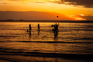 Silhouette of children playing with a ball by the river, golden sunset reflecting in the water