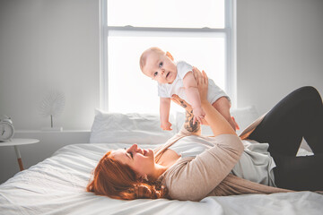 young beautiful mother with a baby boy on the bed at home - obrazy, fototapety, plakaty