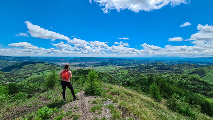 Hiker woman on rock formation along idyllic hiking trail through lush green forest in Grazer Bergland, Prealps East of the Mur, Styria, Austria. Vibrant green leaves. Soft hills in alpine landscape