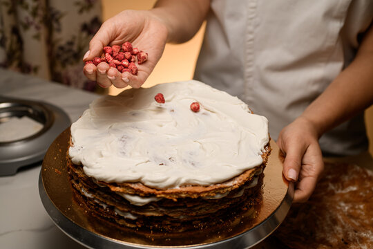 Baker holds dried strawberries in his hand near the cake