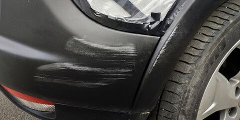 Plastic car bumper with a scratch, under the black bumper of a car. - obrazy, fototapety, plakaty