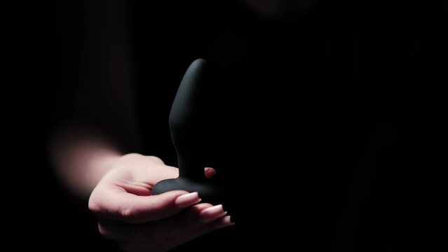Silicone anal vibrator with a remote control in a female hand on a black background. Massager with multiple speeds. Products for intimate shops, adult gifts for couples
