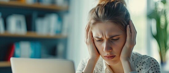 Young frustrated woman working at office desk in front of laptop suffering from chronic daily headaches treatment online appointing to a medical consultation electromagnetic radiation sick pay - obrazy, fototapety, plakaty