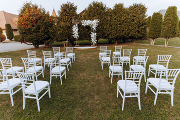 Decor at the wedding. Many white chairs and a golden arch decorated with white flowers