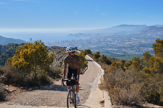 Man cyclist riding a bike with beautiful view on Benidorm, Costa Blanca, Spain. Man cyclist wearing cycling kit and helmet. Sports motivation image. Cycling through stunning Spanish mountain landscape