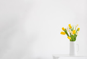 white and yellow spring flowers  in vase on white background - obrazy, fototapety, plakaty