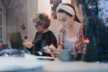 Two women focused on their individual tasks in a cozy cafe setting, exuding a vibe of productivity and concentration. - obrazy, fototapety, plakaty