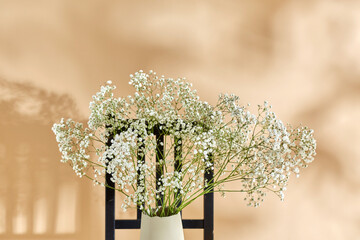 home decor and design concept - close up of gypsophila flowers in vase on vintage chair over beige...