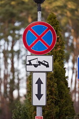 Znak zakazu parkowania i informacja o holowaniu, w tle las