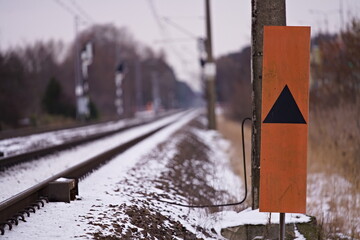 Znak kolejowy obok torów pokrytych śniegiem w zimowy dzień - obrazy, fototapety, plakaty