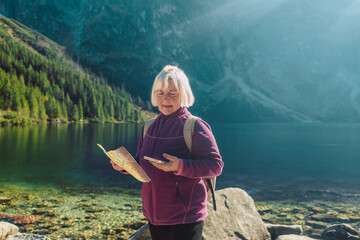 Shot of a senior 60s lost woman with smart phone holding a map while taking in the view from the...