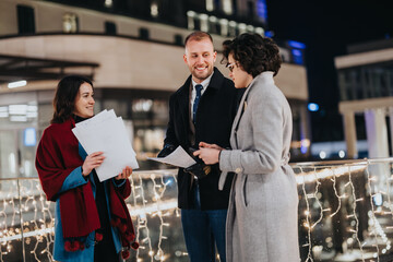 Young colleagues engaging in a casual business discussion at night, illuminated by surrounding festive lights, showcasing teamwork.