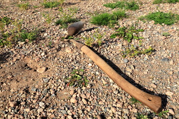 Old style hoe or pickax. Wooden tool on the ground. Summer day outside.