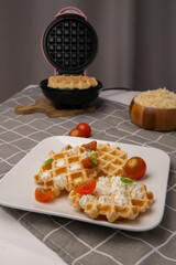 Homemade Belgian cheese waffles served as a Healthy snack. waffles with cottage cheese, cherry tomatoes and basil leaf, presented on a wooden board for a healthy breakfast.
