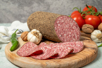 Peppered salami and slices on cutting board. Italian salami with pepper on gray background. Close up