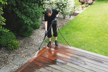 man cleaning terrace with a power washer - high water pressure cleaner on wooden terrace surface - obrazy, fototapety, plakaty