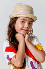 Close-up portrait of little cute girl in straw hat resting her hands on her face on white background