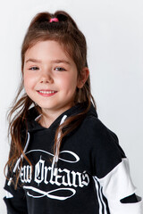 Close-up portrait of little stylish smiling kid girl wearing a black hoodie on white studio background
