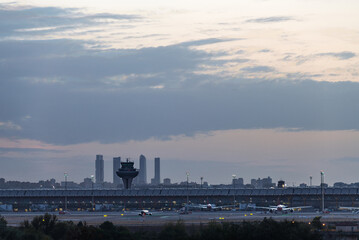 Panorama view of the T4 terminal of Madrid Barajas airport at dusk, with the skyline of the city and its four skyscrapers in the background. - 743151564