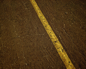 Worn out and cracked old asphalt of a highway with a yellow divide line. Detail shot. - 743154725