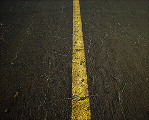 Worn out and cracked old asphalt of a highway with a yellow divide line. Detail shot. - 743154795