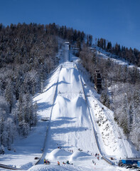 Giant Planica Ski Jump with Snow-Covered Slopes on a clear sunny winter day. People playing on snow at the bottom of the ski jump - 743156705