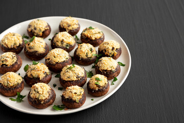 Homemade Garlic Parmesan-Stuffed Mushrooms on a plate on a black background, side view. Copy space.
