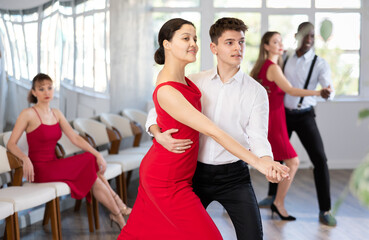 Fototapeta na wymiar Smiling couple enthusiastically dancing social latin cha-cha-cha dance in modern dance salon