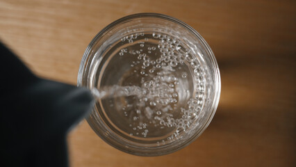 Pouring clean drinking water into a glass. View from above. Close-up of pouring fresh drinking water into a glass on a wooden table. Drink concept, healthy