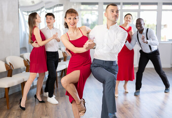 Fototapeta na wymiar Happy caucasian man and girl in red dress dancing rock and roll dance in modern dance studio during celebration or party