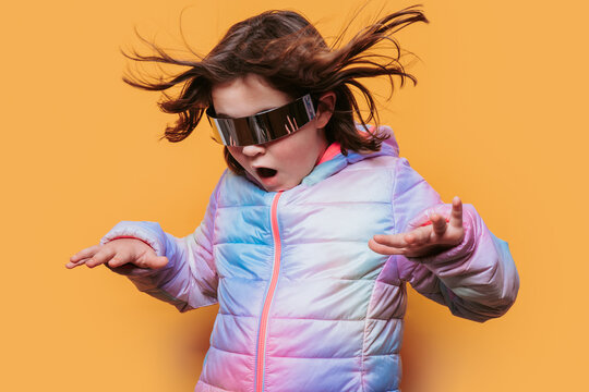 Child in awe with hair flying, wearing sleek futuristic glasses and a colorful jacket against an orange background