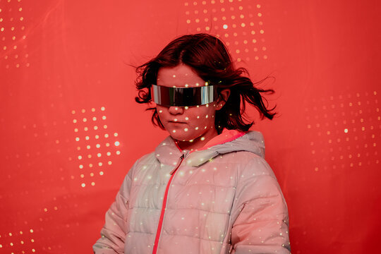 Girl with a serious expression, sporting reflective futuristic glasses and a white puffer jacket, against a dotted red backdrop