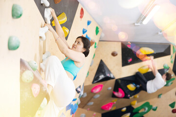 Asian girl is focused on clambing to top of artificial climbing wall along complicated route track...