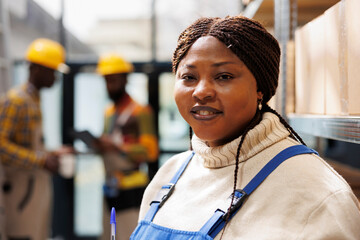 Smiling african american woman working in industrial warehouse portrait. Shipment manager with...