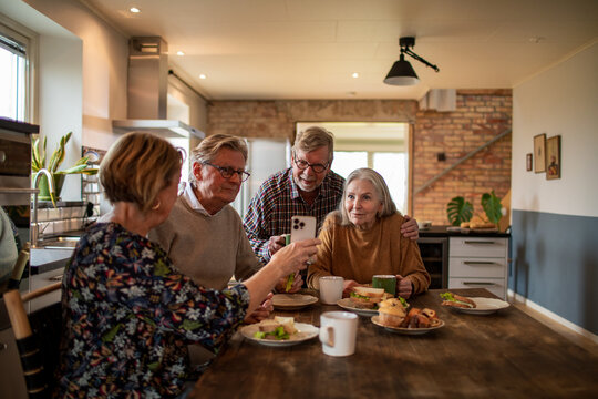 Group of senior people using smartphone together at kitchen table