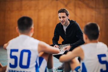 A basketball coach is working on game plan with his junior team on court.
