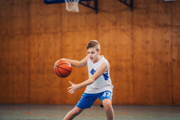 Dynamic portrait of junior basketball player dribbling a ball on court.