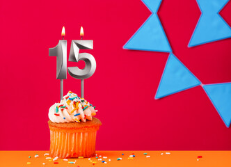 Birthday cupcake with candle number 15 on a red background with blue pennants