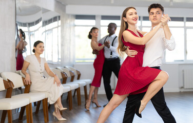 Expressive handsome young guy in formal wear and graceful woman in vibrant red dress rehearsing...