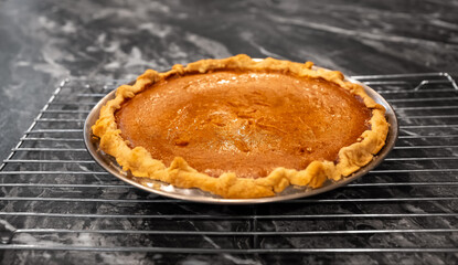 Home made and fresh baked pumpkin pie, waiting to be eaten as it sits on a metal cooling rack on the kitchen counter.