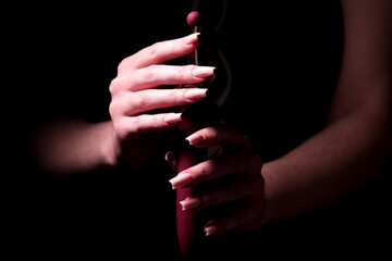Burgundy stylish dildo for masturbation in a girl’s hand on a black background. Nozzle for...