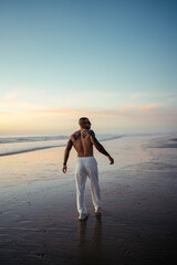 Chico joven tatuado y musculoso posando sin camiseta en la playa al atardecer