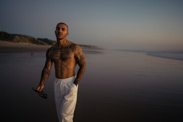 Chico joven musculoso y tatuado posando isn camiseta en la playa y en la calle