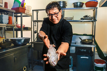Chef in the restaurant kitchen with a fish in hand, the catch of the day. Seafood. Kitchen...