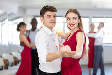 Obraz premium Positive dancing couple enjoying social dance during group party in modern sport dance studio