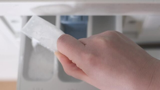 Female hand pours a scoop of powder into washing machine, top view.