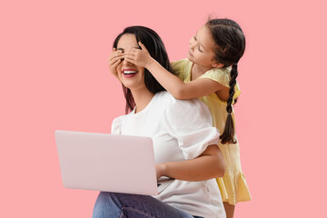 Little girl covering her working mother's eyes on pink background