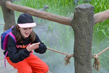 A young girl in a pink hat and black hoodie sits under a tree with a lee logo - Powered by Adobe