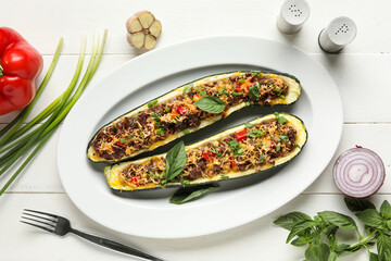 Plate with meat stuffed zucchini boats and fresh vegetables on white wooden background